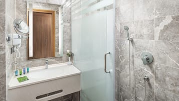 A modern bathroom with a glass shower enclosure, a wooden door, and a marble-tiled wall.