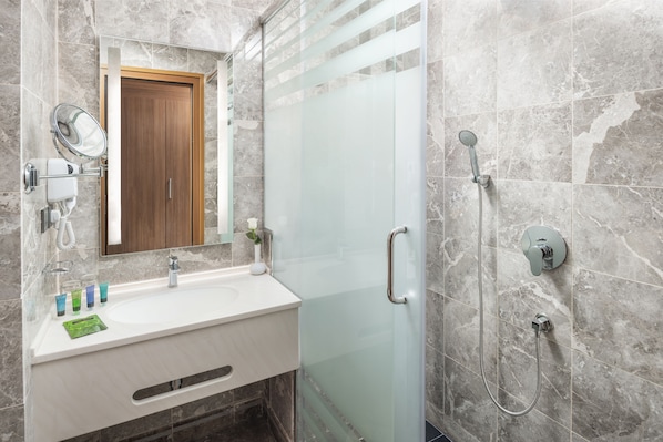 A modern bathroom with a glass shower enclosure, a wooden door, and a marble-tiled wall. - Three Pearls Musalli Makkah (Makkah)