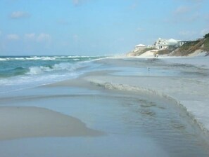 Une plage avec des vagues, une étendue de sable et des bâtiments en arrière-plan.