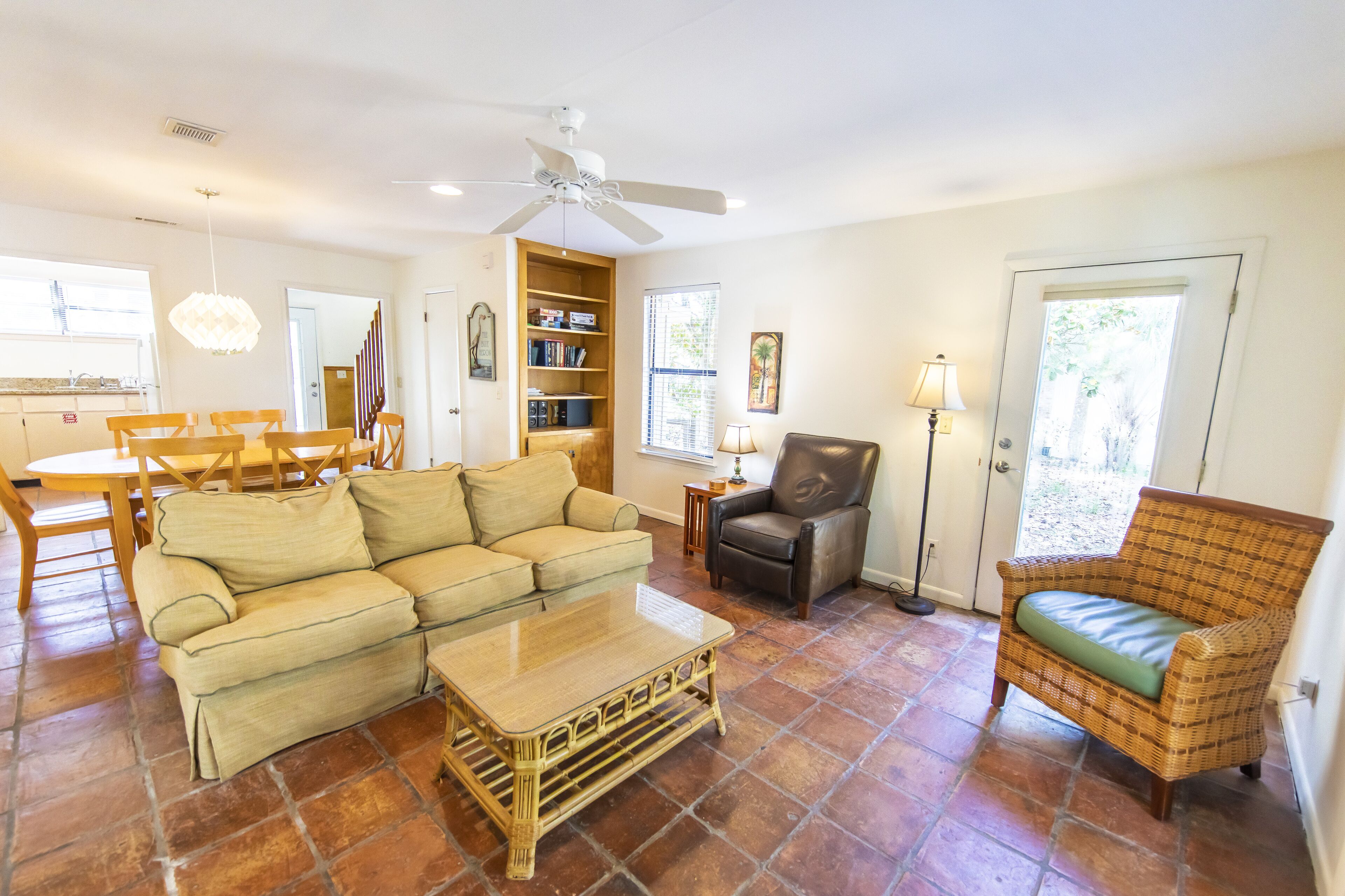 A living room with a sofa, coffee table, and two chairs. There is a bookshelf, a lamp, and a ceiling fan.