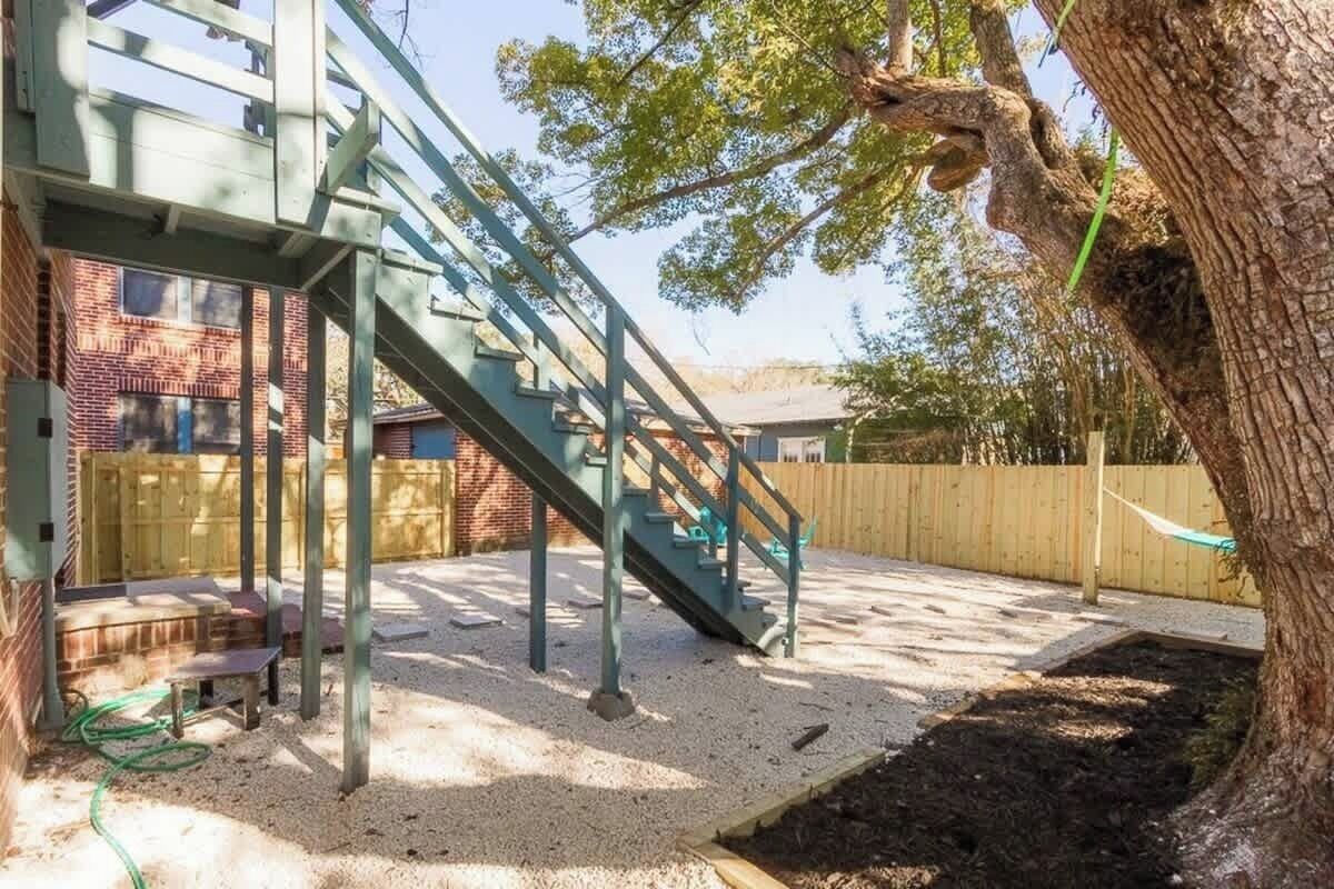 Un patio trasero con una escalera metálica, una valla de madera y un árbol.