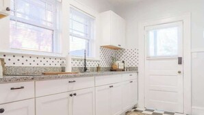 Cozinha com armários brancos, tapete estampado e piso xadrez.