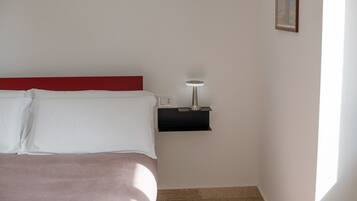A neatly made bed with white and pink bedding, a small bedside table with a lamp, and a framed picture on the wall.