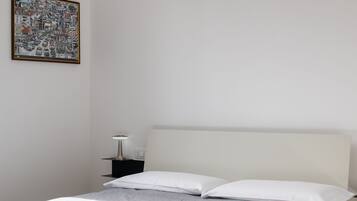Un dormitorio con una cama, dos almohadas, una mesita de noche con una lámpara y un cuadro enmarcado en la pared.