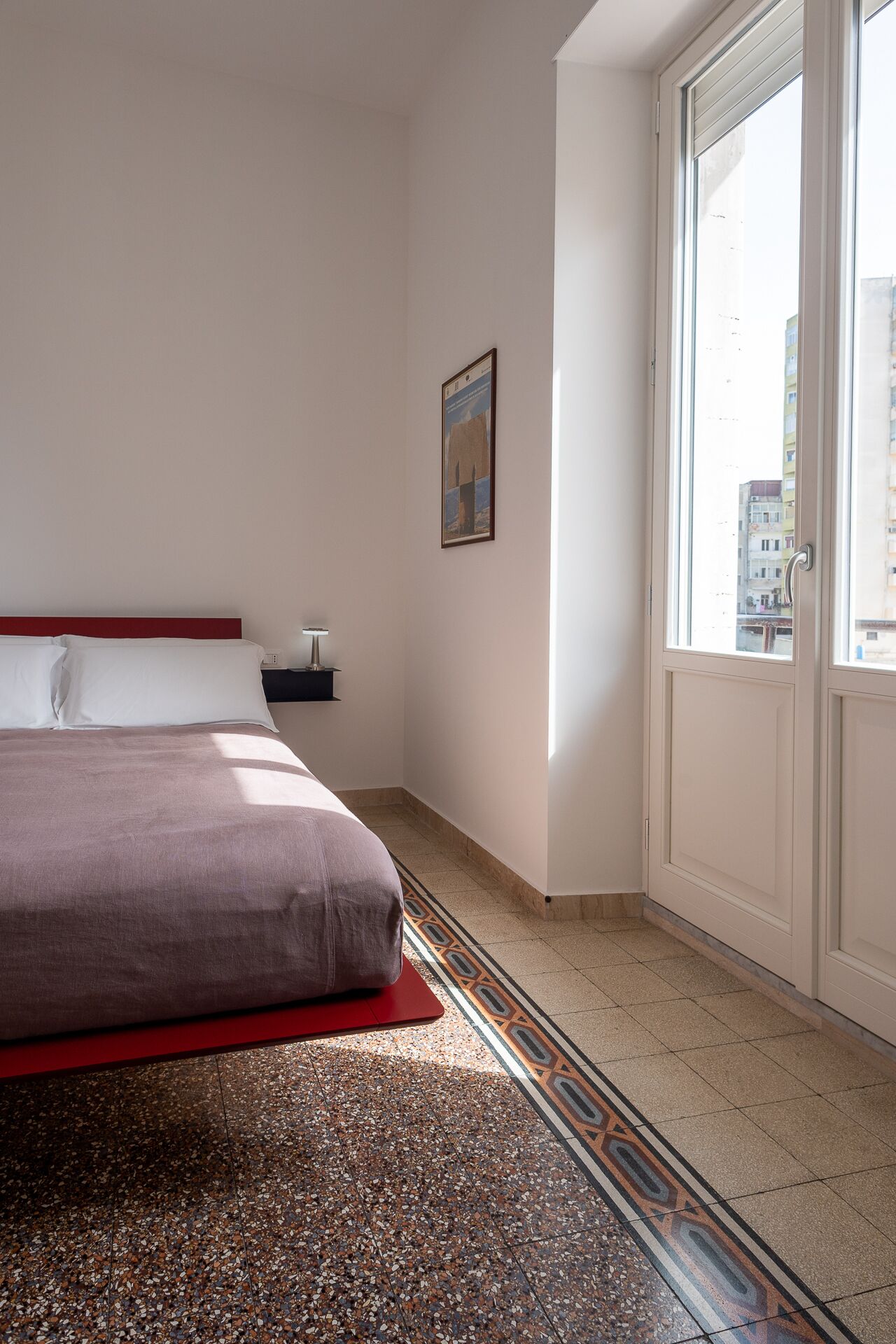 A hotel room with a bed, a nightstand, a window, and a door.