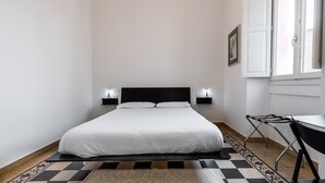 Een keurig opgemaakt slaapkamer met een bed, bedlampjes, een klein tafeltje en een raam.