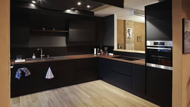 A modern kitchen with dark cabinetry, a wooden countertop, a built-in oven, and a large mirror above the sink.