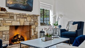 Una sala de estar con chimenea de piedra, un sillón azul cómodo, una mesa de centro y un cuadro grande en la pared.