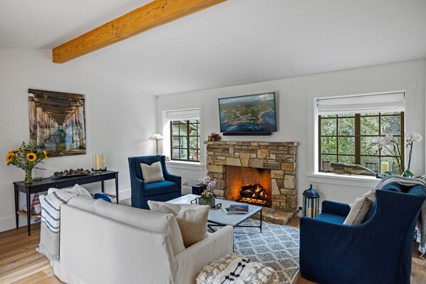 Ein Wohnzimmer mit Kamin aus Stein, blauen Sesseln, einem weißen Sofa und Kunstwerken an den Wänden.
