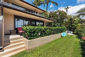 A modern house with a covered patio, a well-maintained lawn, and a surfboard. - Captivating Oceanfront Ground-Floor Gem - Makena Surf G-101 - Gorgeous Views! (Makena, Maui)
