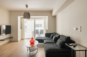 Ein modernes Wohnzimmer mit grauem Sofa, rundem Couchtisch mit roter Vase, Flachbildfernseher und Pendelleuchte.