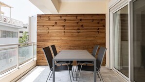 Un balcon avec un mur en bois, une table en métal avec quatre chaises et une porte-fenêtre coulissante.