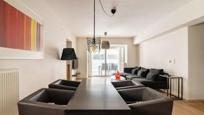 Un salon moderne avec une longue table, des fauteuils en cuir noir, un canapé noir et un grand tableau abstrait accroché au mur.