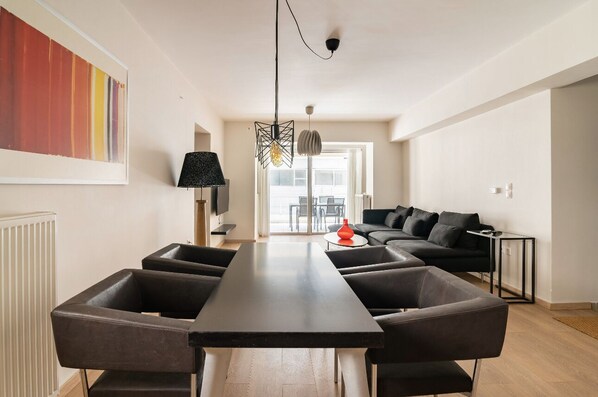 Ein modernes Wohnzimmer mit einem langen Tisch, schwarzen Ledersesseln, einem schwarzen Sofa und einem großen abstrakten Gemälde an der Wand.