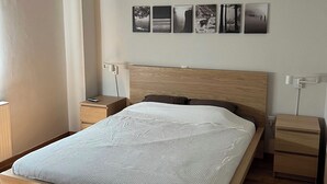 Une chambre à coucher moderne avec un lit en bois, des tables de chevet, un climatiseur fixé au mur et un luminaire au plafond.