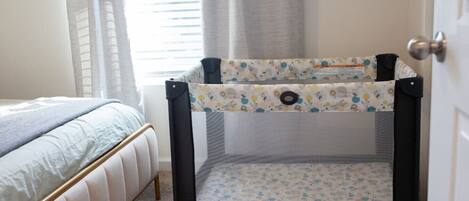 Une pièce avec un lit, un parc pour bébé de la marque Graco et une porte.