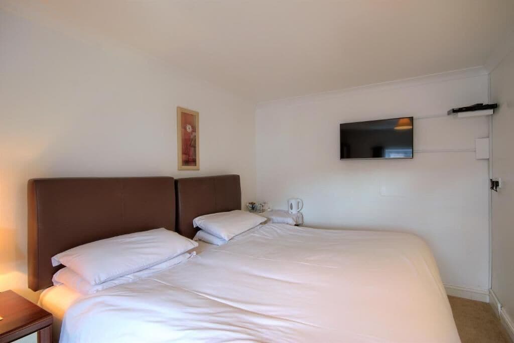 A hotel room with a large bed, a flat-screen TV mounted on the wall, and a small bedside table with a lamp.