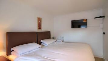 A hotel room with a large bed, a flat-screen TV mounted on the wall, and a small bedside table with a lamp.