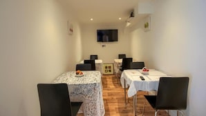A dining area with tables and chairs, a flat-screen TV mounted on the wall, and a framed picture on the wall. - Mount Lavinia (Sheringham)