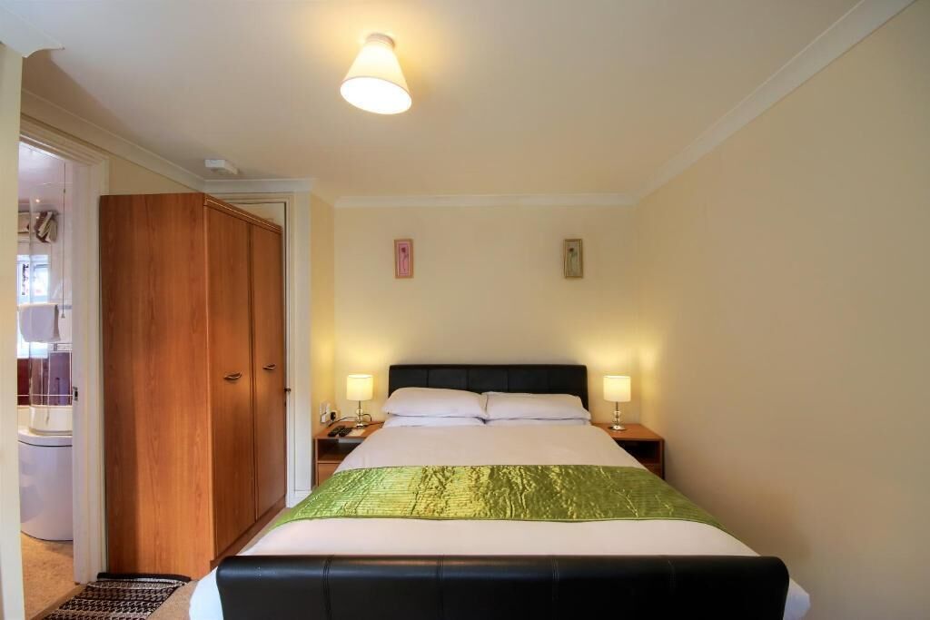 A hotel room with a bed, bedside lamps, a wardrobe, and a bathroom visible through an open door.