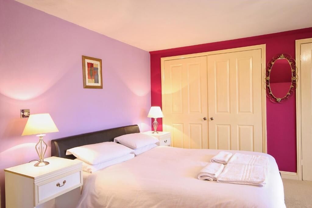 A bedroom with a bed, two bedside tables with lamps, a nightstand, a large wardrobe, and a mirror on the wall.