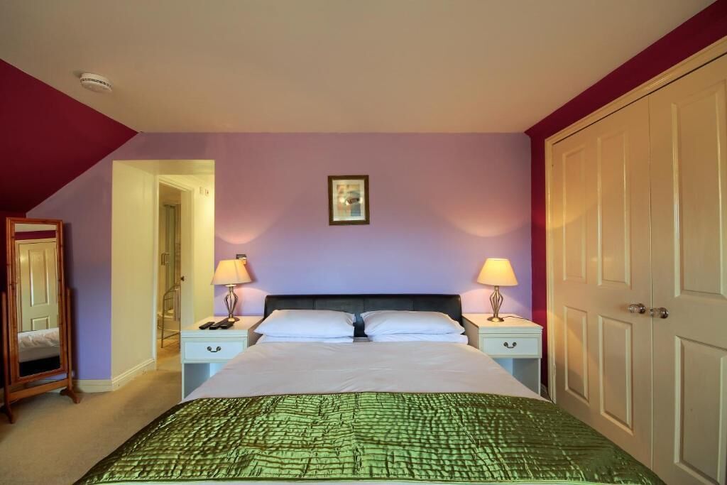 A bedroom with a bed, two bedside tables with lamps, a framed picture on the wall, and a wardrobe.
