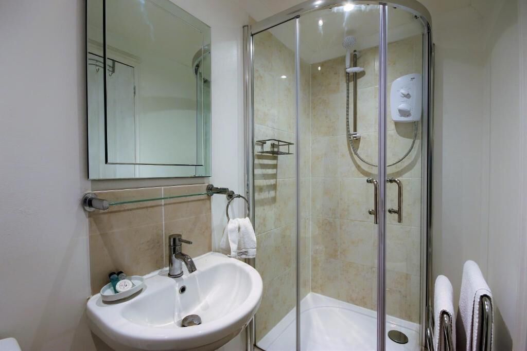 Un baño moderno con ducha de vidrio, lavamanos blanco y espejo sobre él.