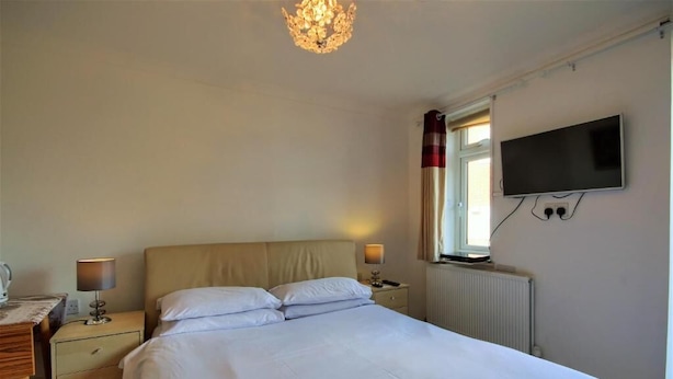 A bedroom with a bed, bedside lamps, a TV mounted on the wall, and a window with curtains. - Mount Lavinia (Sheringham)
