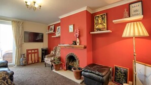 A living room with a fireplace, red walls, and various decorative items. - Mount Lavinia (Sheringham)