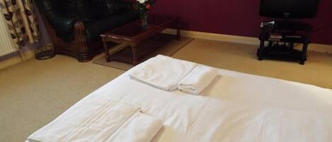 Habitación de hotel con cama, sofá de cuero, una mesita con un jarrón de flores y un televisor sobre un mueble.