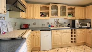 A kitchen with wooden cabinets, a microwave, a toaster, and a refrigerator. - Mount Lavinia (Sheringham)