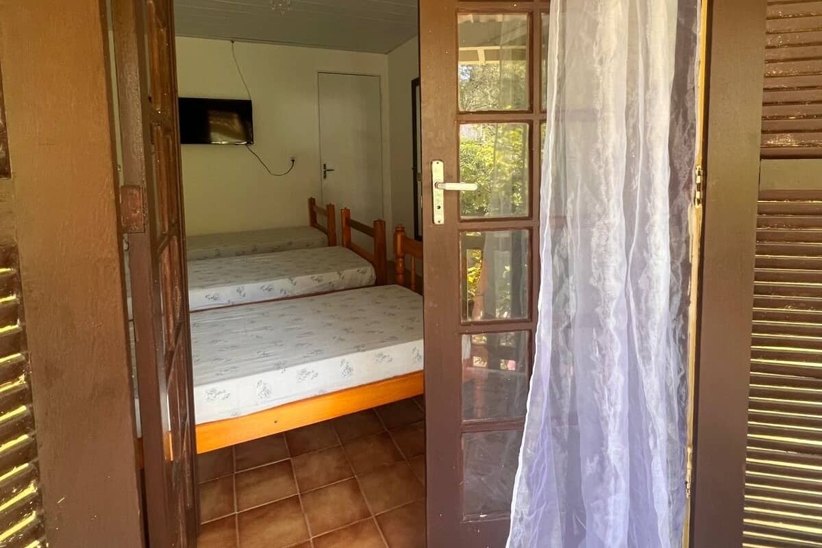 Un petit logement composé d’une seule pièce, comprenant un lit, une fenêtre avec des rideaux et une porte.