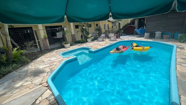 Una piscina con dos personas sobre balsas inflables, rodeada de baldosas de piedra y plantas en macetas.