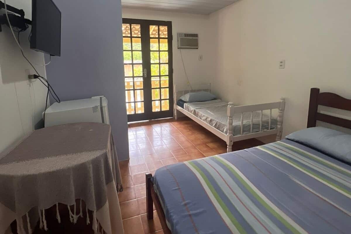 Une chambre à coucher avec un lit, une petite table, un téléviseur fixé au mur et une fenêtre donnant sur l’extérieur.