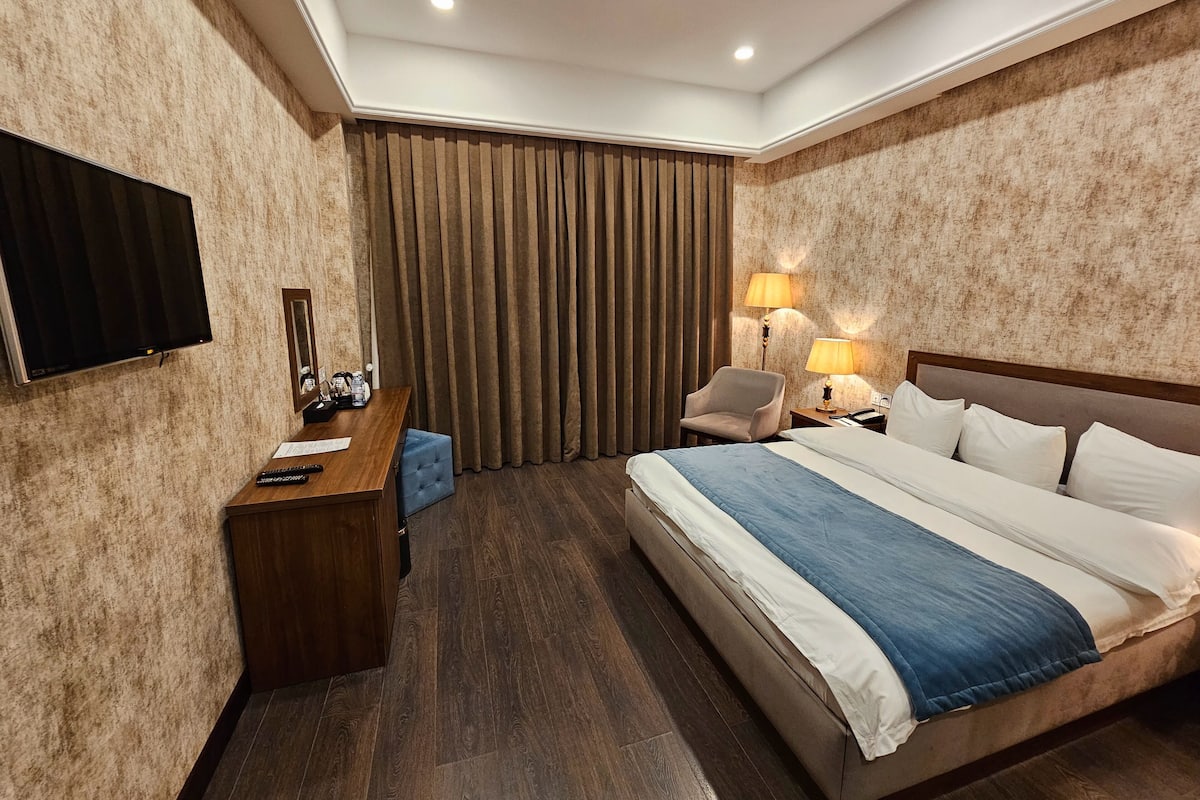 A hotel room with a bed, desk, chair, and a television.