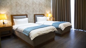 Una camera d'albergo con due letti, una testiera in legno, un comodino con una lampada e un'ampia finestra con tende.
