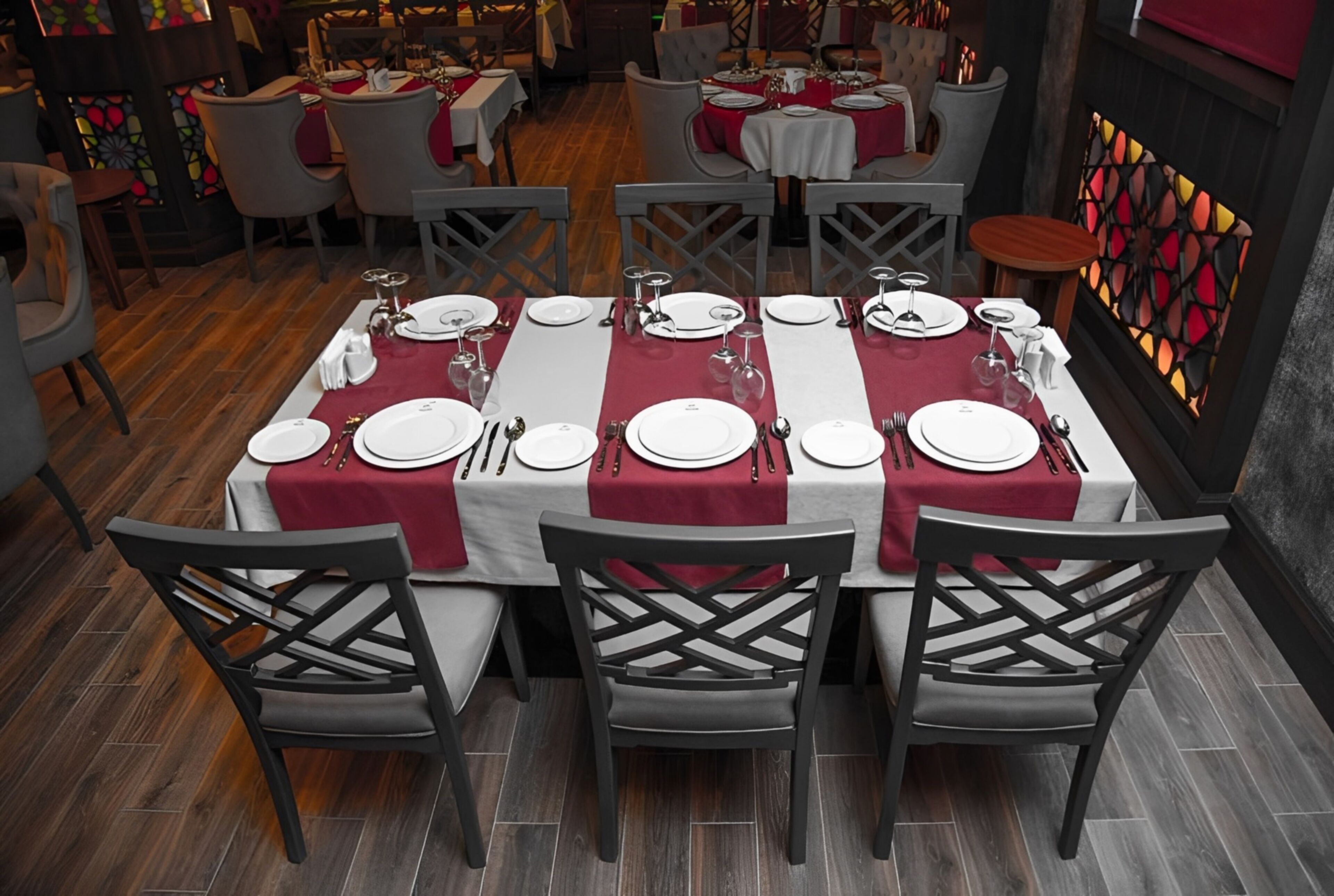 Un restaurante con mesas dispuestas para comer, con mantel rojo y platos blancos.