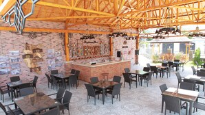 Ristorante all'aperto con pareti in mattoni, travi in legno e zona bar. Tavoli e sedie disposti per la ristorazione.