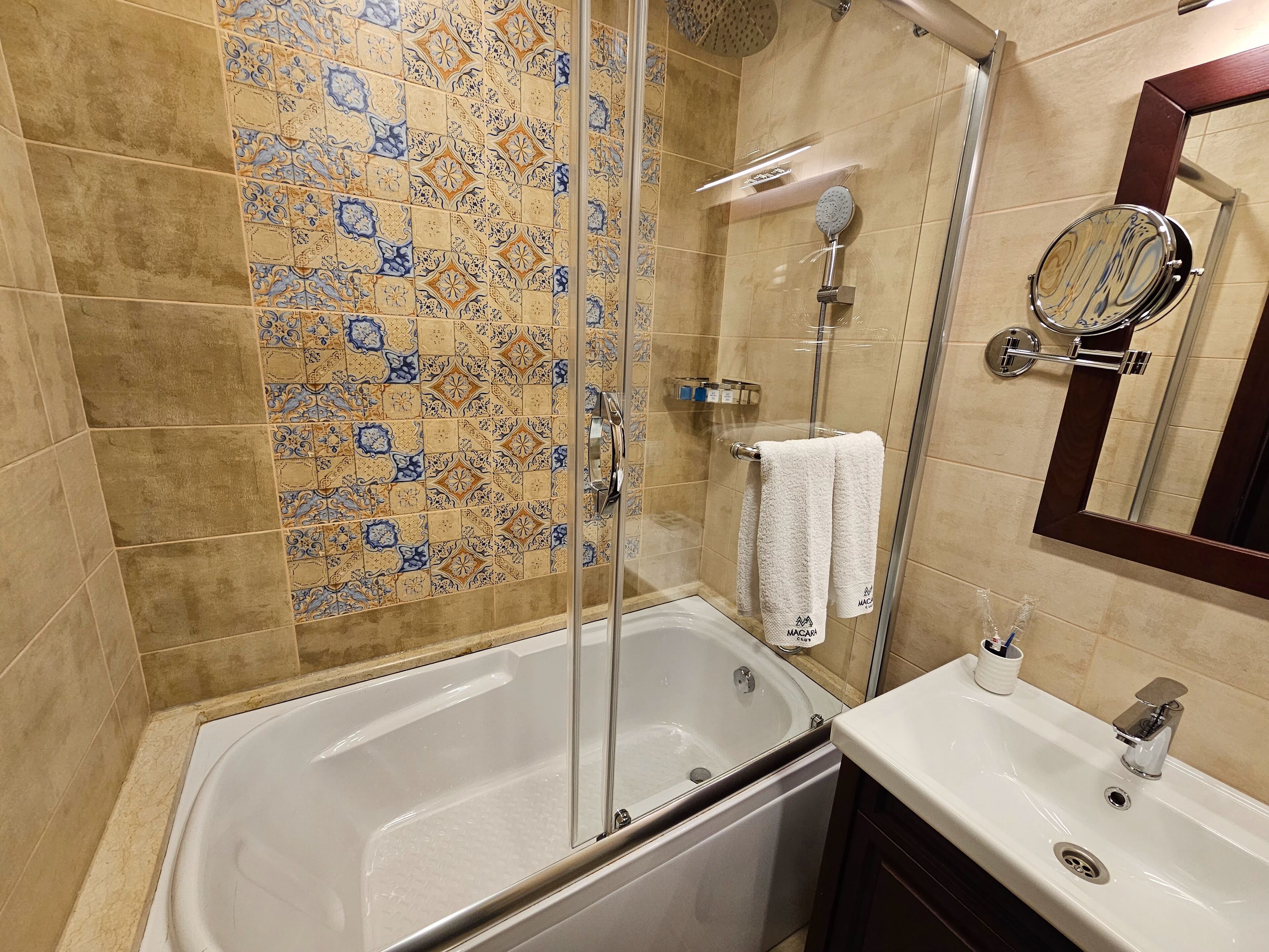 Un baño con bañera, ducha con mampara de vidrio, lavamanos y espejo.