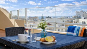 Un balcón con una mesa lista para el desayuno, una jarrón, un florero y vistas a edificios.