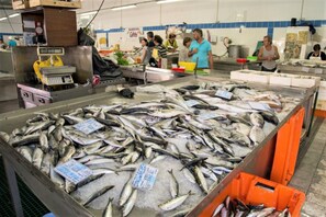 Un mercato di pesce con diversi tipi di pesce esposti su ghiaccio, una bilancia e persone che fanno acquisti.