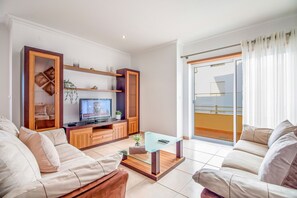 A modern living room with a sofa set, a coffee table, a TV, and a balcony with a view. - Apartament Alameda | 2 Bedrooms | Spacious Balcony | Quarteira (Quarteira)