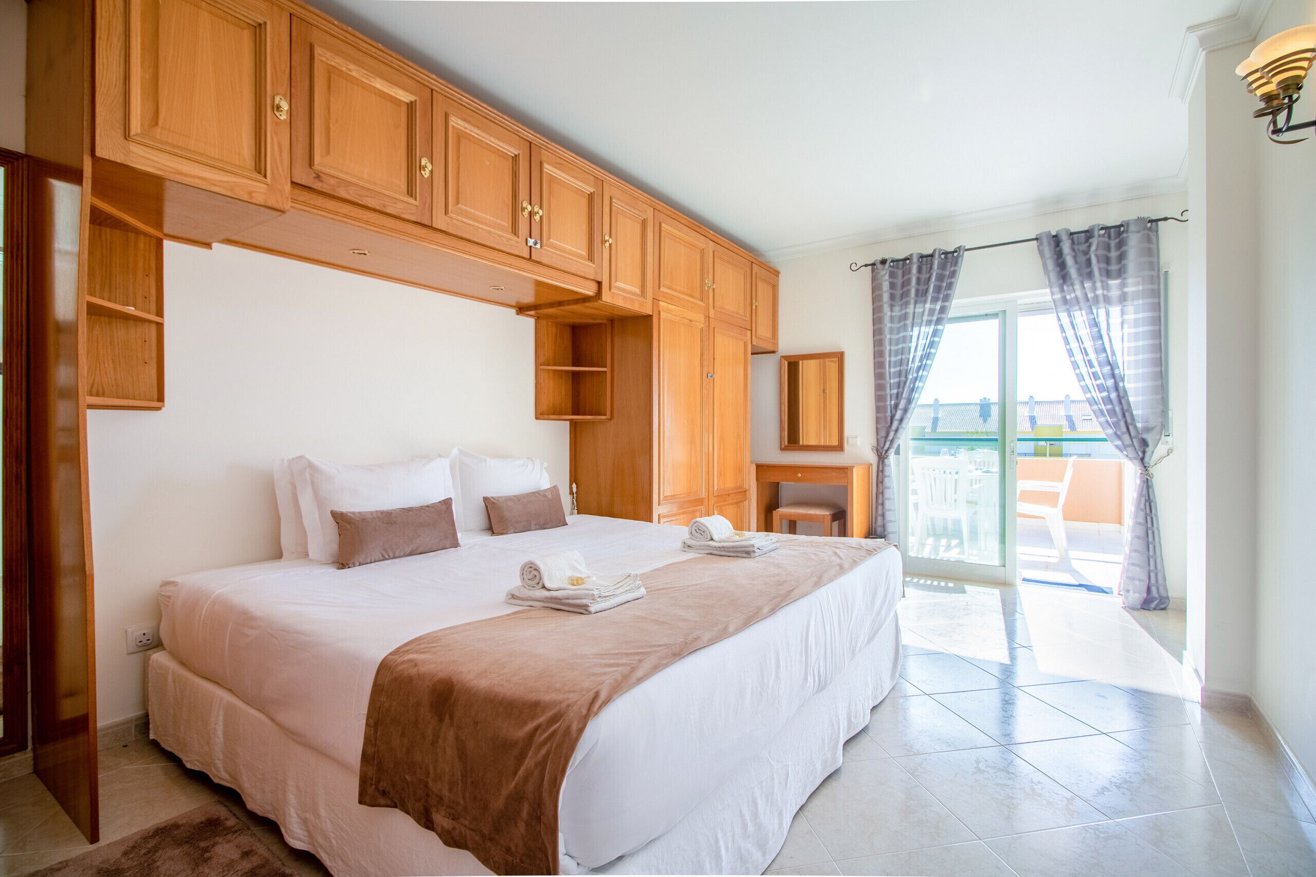 Una camera da letto con un letto grande, mobili in legno, un tavolino e un balcone con tende.