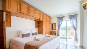 Un dormitorio con una cama grande, armarios de madera, una mesita y un balcón con cortinas.