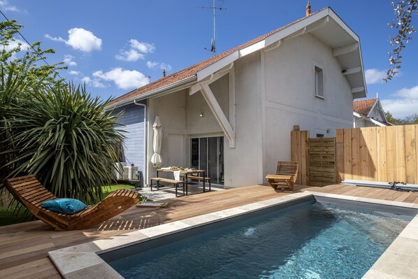 Une maison moderne dotée d’une piscine, d’une terrasse en bois et de mobilier d’extérieur.