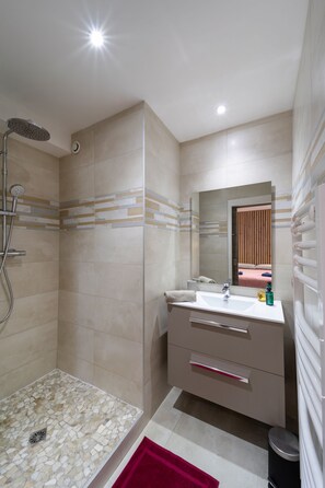 Une salle de bain moderne équipée d’une douche, d’un lavabo avec miroir et d’un meuble-lavabo avec tiroirs.