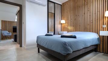 Une chambre d’hôtel moderne dotée d’un grand lit, d’un mur revêtu de panneaux en bois et d’un coin salon avec une chaise et une table.