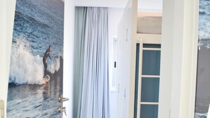 A hallway with a wooden floor, a large painting of a surfer on a wave, and a blue door with a glass panel. - Hostel AzorAzul (Ponta Delgada)
