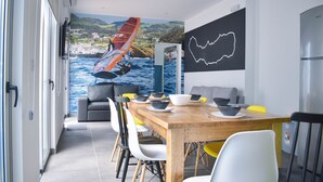 A modern dining area with a mural of a windsurfing scene, a wooden table set for dining, and a minimalist wall art piece. - Hostel AzorAzul (Ponta Delgada)