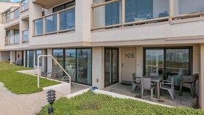 Un immeuble résidentiel à plusieurs étages doté d’un balcon, de portes vitrées et d’un espace extérieur aménagé pour s’asseoir.